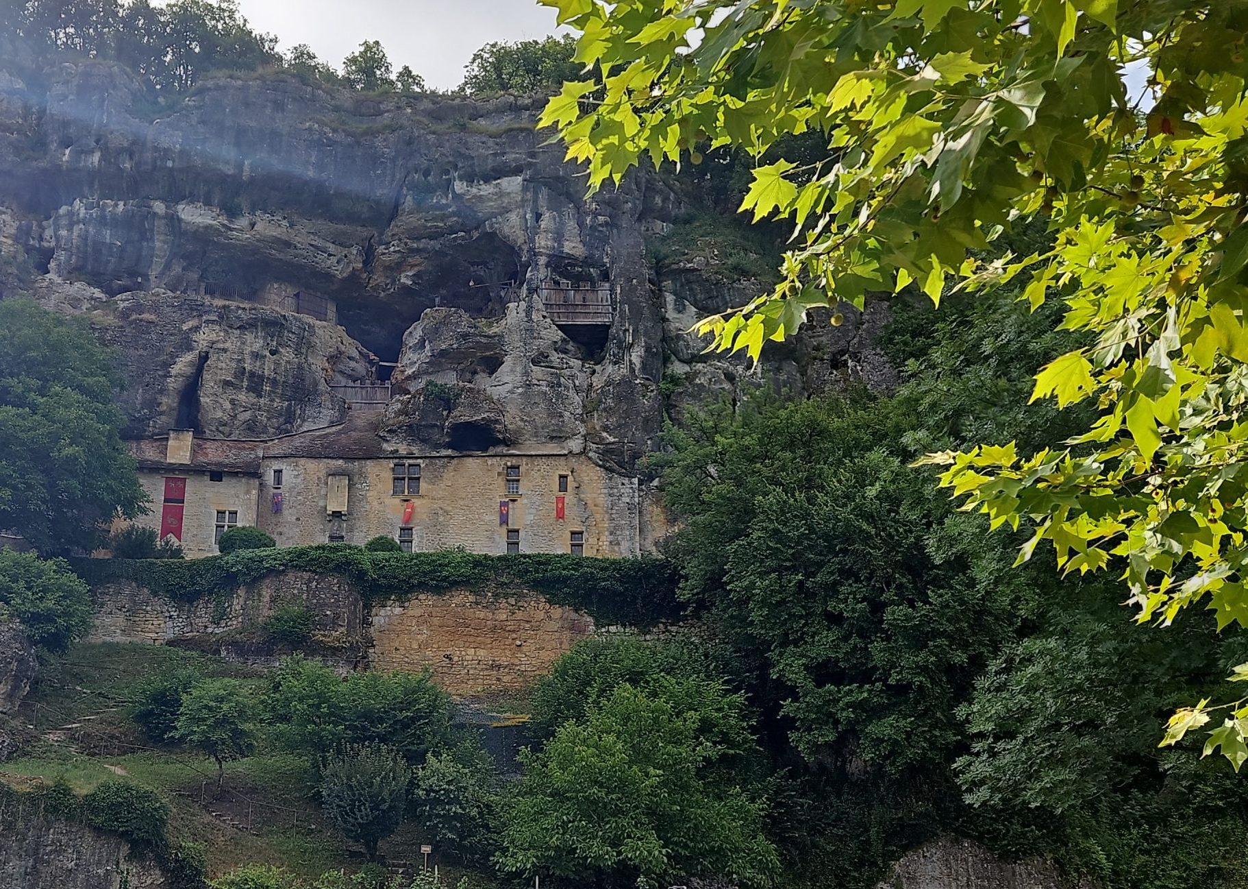 Vista exterior de la Maison Forte de Reignac, un castillo-acantilado parcialmente construido en una cueva natural en Dordoña, Francia, rodeado de vegetación.