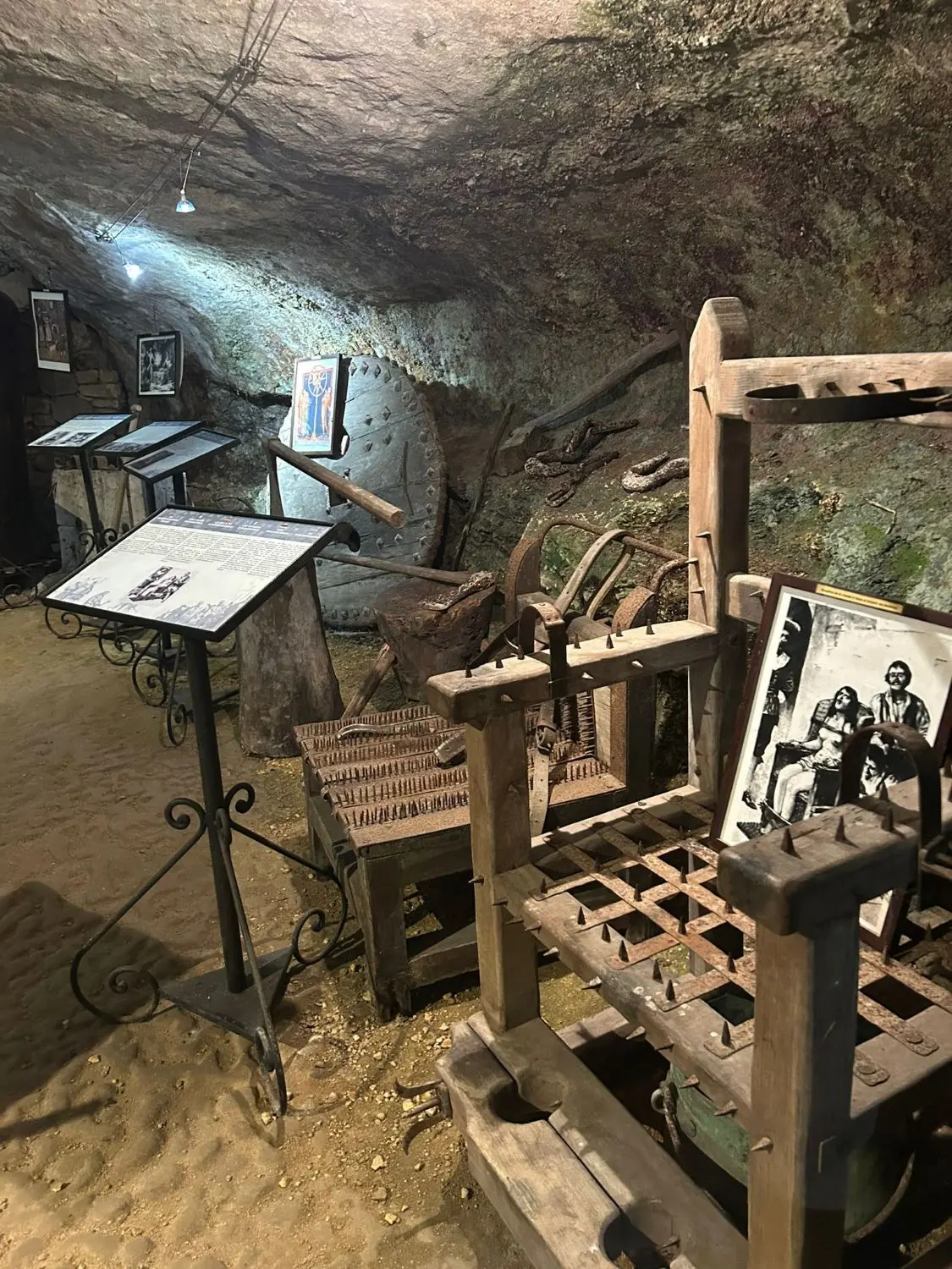 Vista de la sala de exposición de instrumentos de tortura medieval en la Maison Forte de Reignac, mostrando una silla de interrogatorio con pinchos, una rueda y otros artilugios en una sala cueva.