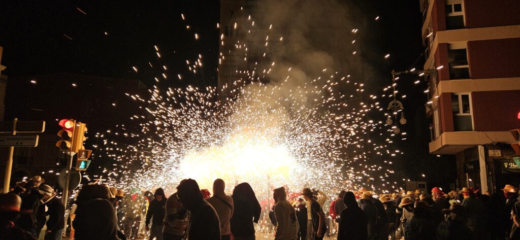 Grupo de Diables de Tarragona lanzando una gran cantidad de chispas y fuegos artificiales en el centro de una calle oscura, rodeados por una multitud de personas durante un Correfoc.