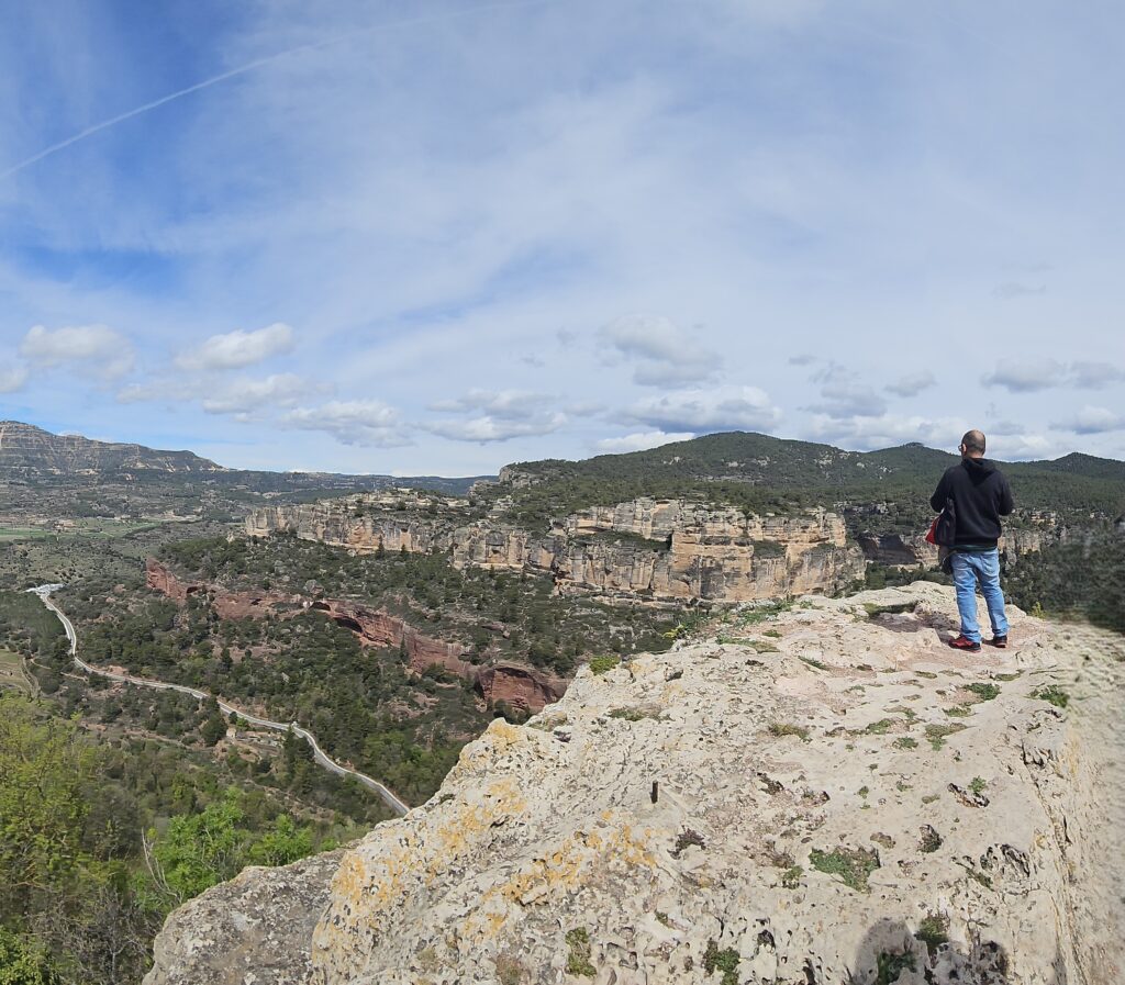 Hombre en la cima de un acantilado de Siurana disfrutando de una vista panorámica épica. Ideal para senderismo, escalada y turismo en las Montañas de Prades, Cataluña.