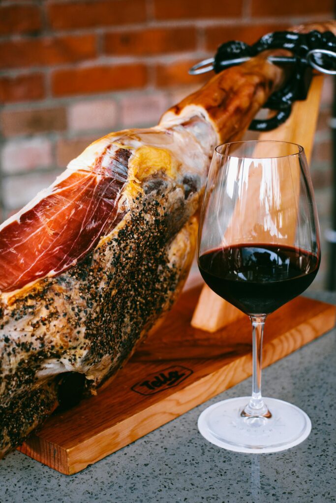Jamón ibérico con una copa de vino tinto sobre soporte de madera, presentación gastronómica elegante y tradicional.