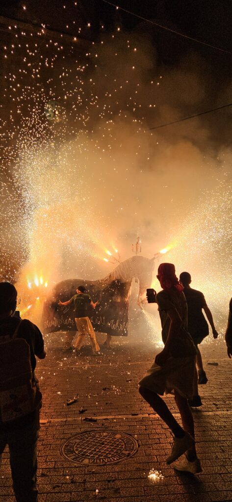 Mulassa de El Vendrell, una figura tradicional de bestia de fuego, en medio de una intensa explosión de chispas y humo durante un Correfoc nocturno en Cataluña. Muestra la silueta de la gente corriendo y bailando alrededor de la figura.