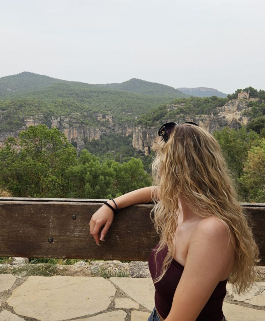 Mujer de espaldas contemplando el horizonte y los acantilados de Siurana desde un mirador de madera al atardecer.