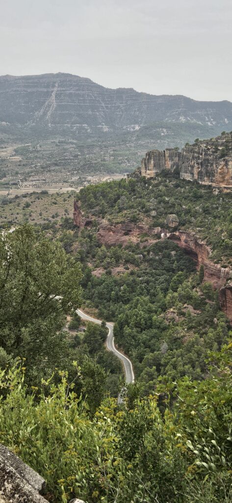 Vista aérea de una carretera sinuosa cruzando un valle frondoso y montañas rocosas en España.