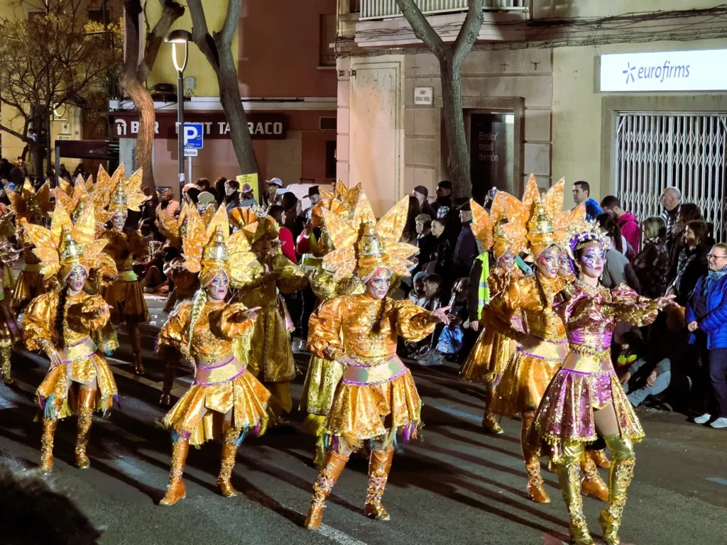 Comparsa desfilando y bailando con llamativos trajes dorados durante la Rua de l'Artesania en el Carnaval de Tarragona.