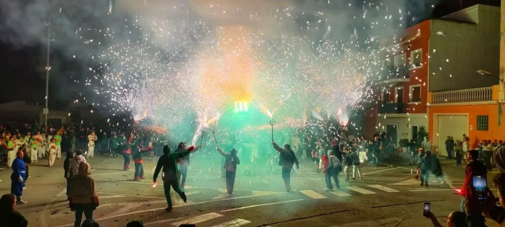 Primer plano vibrante de un diable con cuernos sosteniendo una estructura pirotécnica que expulsa una lluvia intensa y caótica de chispas rojas y naranjas.