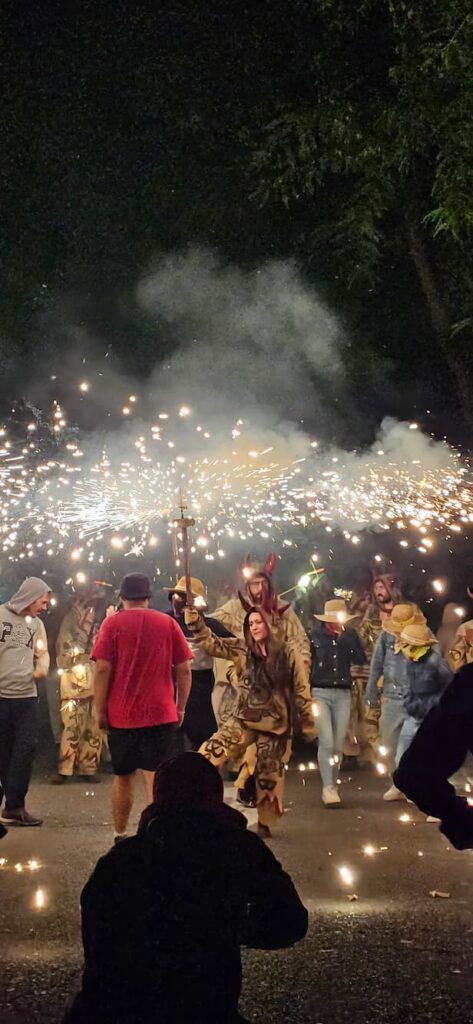 Grupo de diables vestidos con trajes de tela tradicionales y sombreros de paja, haciendo girar pirotecnia y chispas en un Correfoc nocturno.