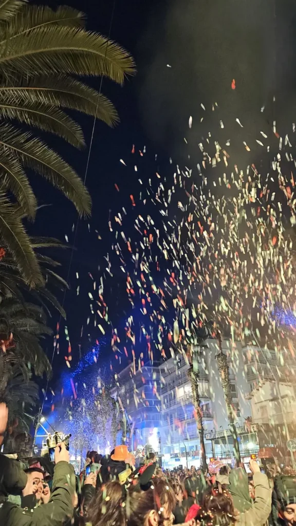 Lluvia masiva de confeti de colores iluminado cayendo sobre la multitud junto a una palmera durante el Cós Blanc de Salou, una intensa fiesta popular de invierno.