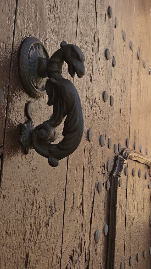 Detalle de un llamador de forja con forma de dragón en una puerta antigua de madera, representando las leyendas locales.