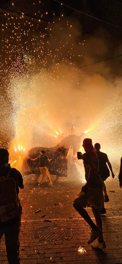 Bestia (mulassa de vendrell) de fuego escupiendo chispas de color naranja oscuro, conocidas como fuego frío, sobre los participantes en un Correfoc.