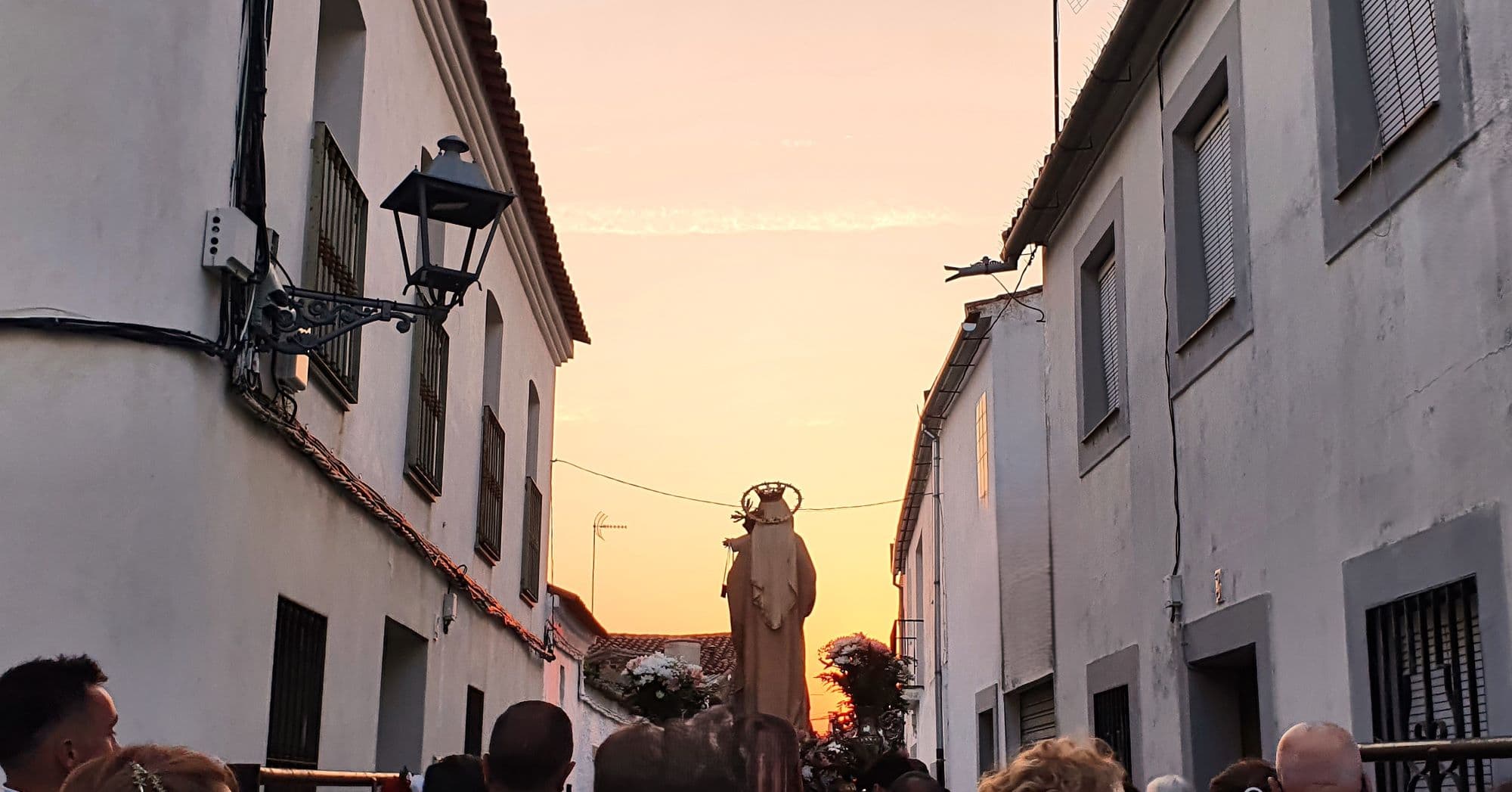 Procesión tradicional de la Virgen al atardecer en una calle estrecha del Valle de los Pedroches, Andalucía.