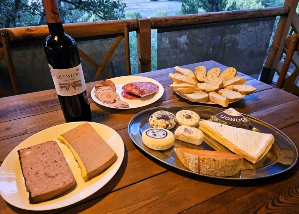 Mesa de madera con tabla de quesos franceses, terrina rústica, embutidos, pan rebanado y botella de vino tinto Ventoux en una terraza al atardecer, en el interior de la provenza francesa
