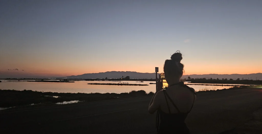 Persona fotografiando el atardecer con un móvil en un paisaje abierto, preparándose para el eclipse solar 2026 en España.